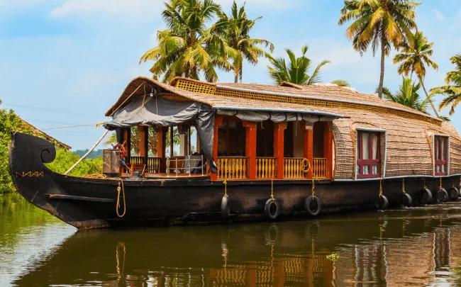 Traditional Kerala houseboat with thatched roof floating on calm backwaters under clear blue skies.