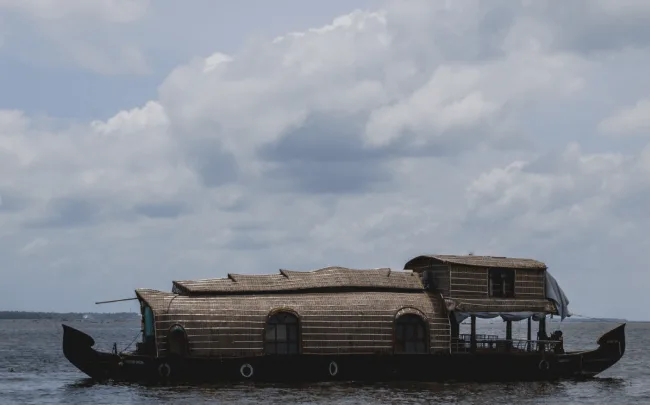 A traditional Kerala houseboat cruising under a cloudy monsoon sky on a wide waterbody.