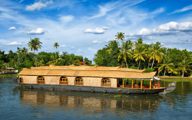 A luxury houseboat trip Alleppey featuring an open-deck Kettuvallam navigating through lush coconut groves.